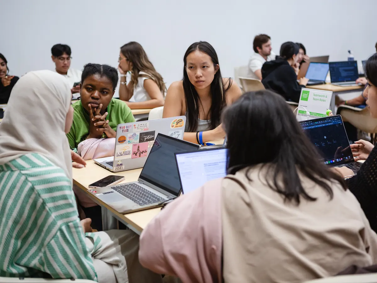 Students working in teams around tables with laptops